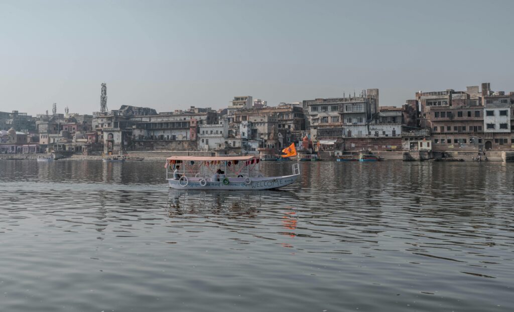 Boat cruising on the Yamuna River with Mathura cityscape in Uttar Pradesh, India.