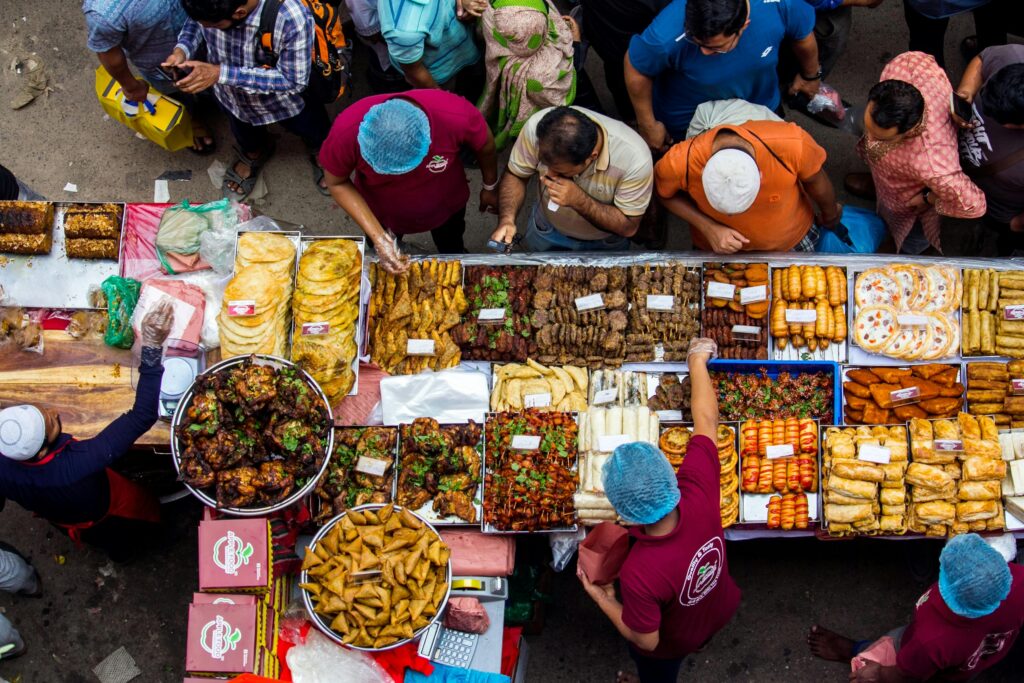 A busy street food market with people buying diverse foods from vendors.